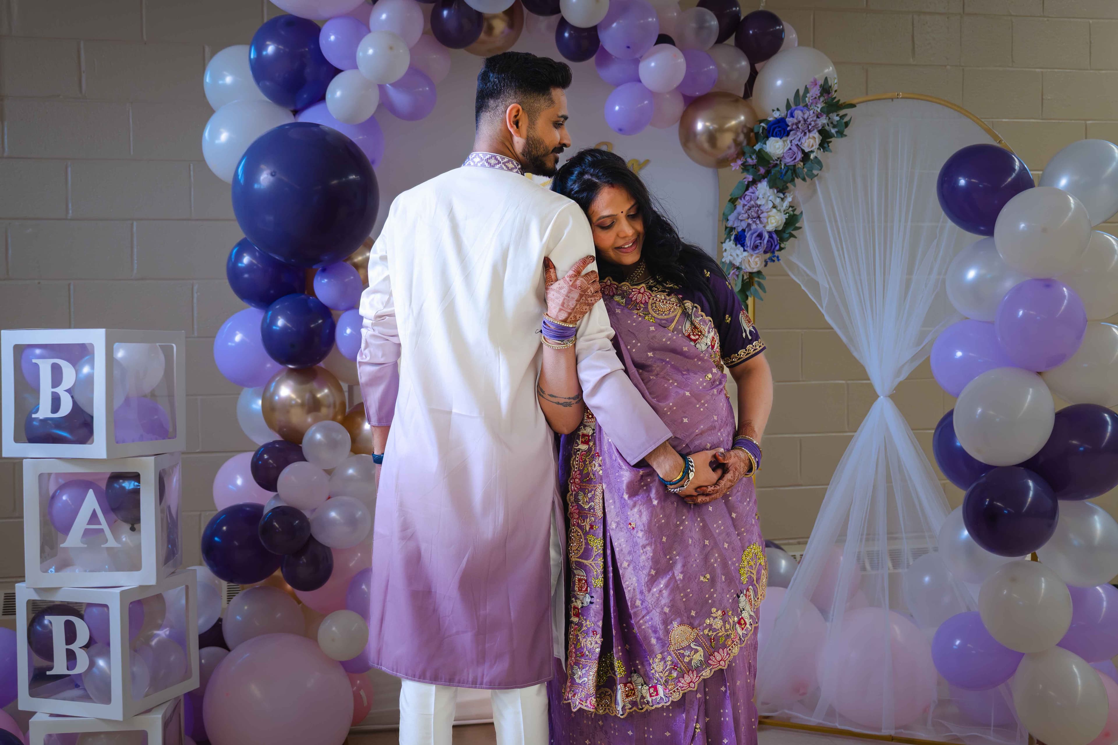 Couple from behind in front of BABY letter blocks and a balloon arch