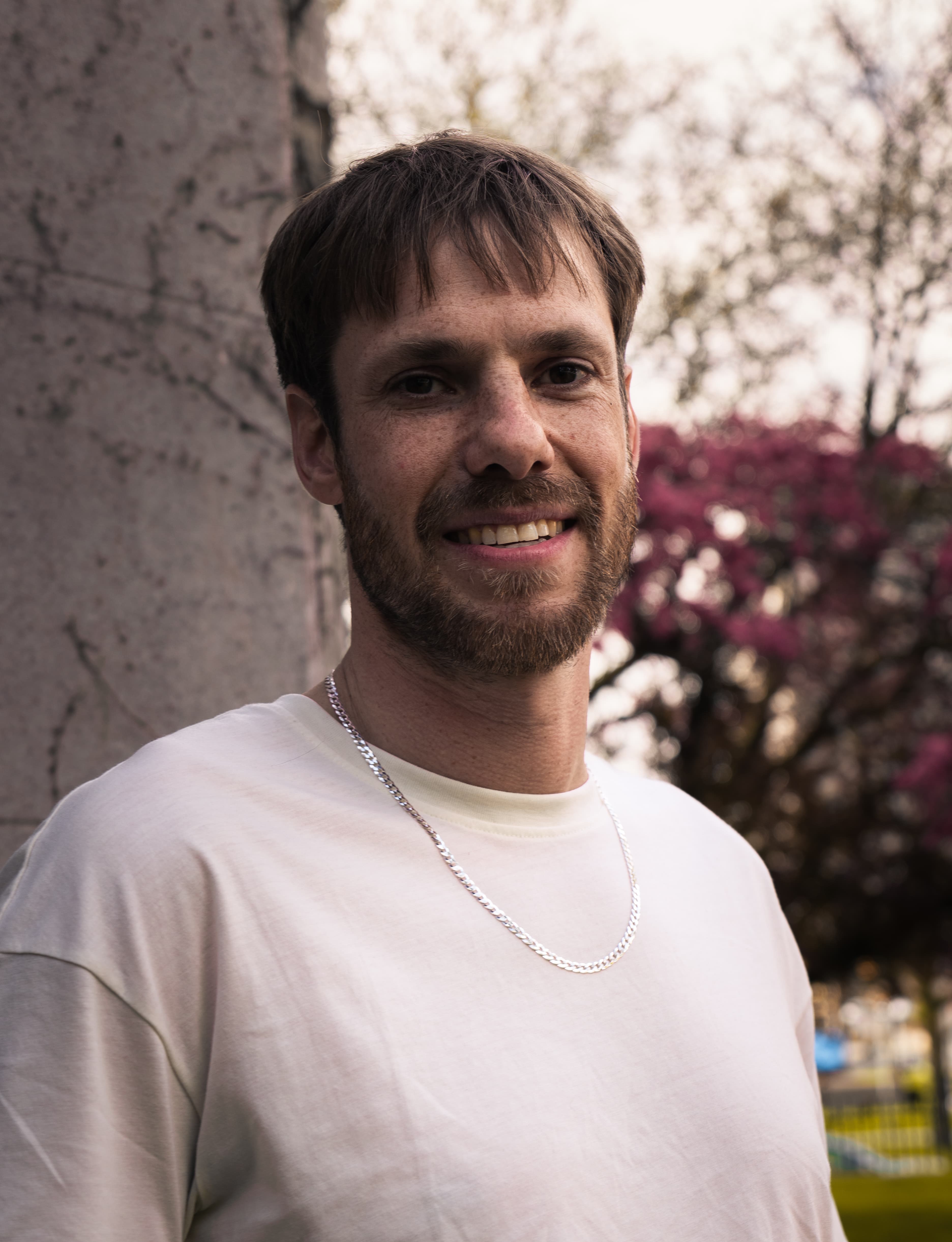 Vertical portrait of a man beside a stone column with pink blossoms behind him