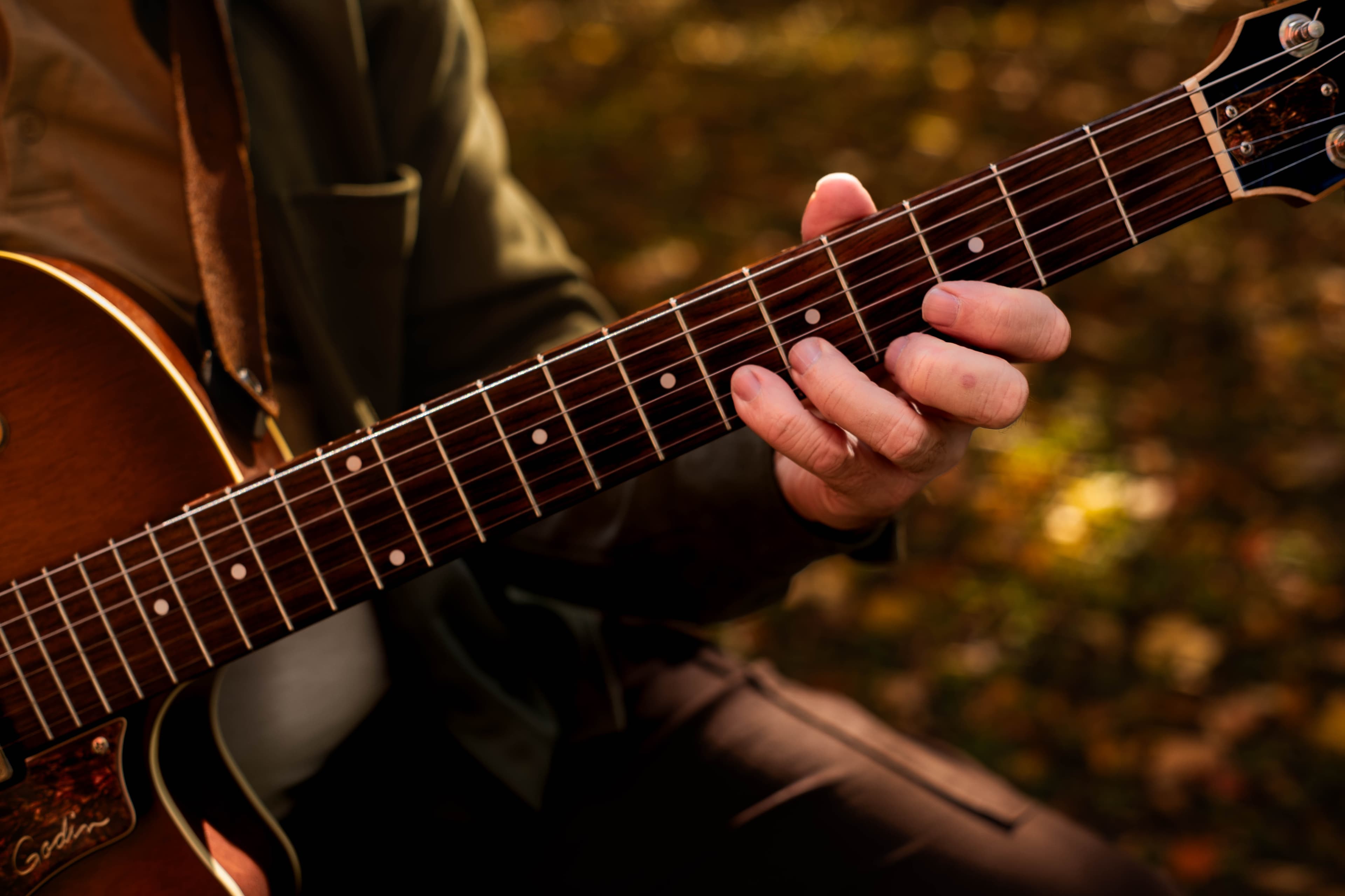 Musician holding an archtop guitar in an autumn forest